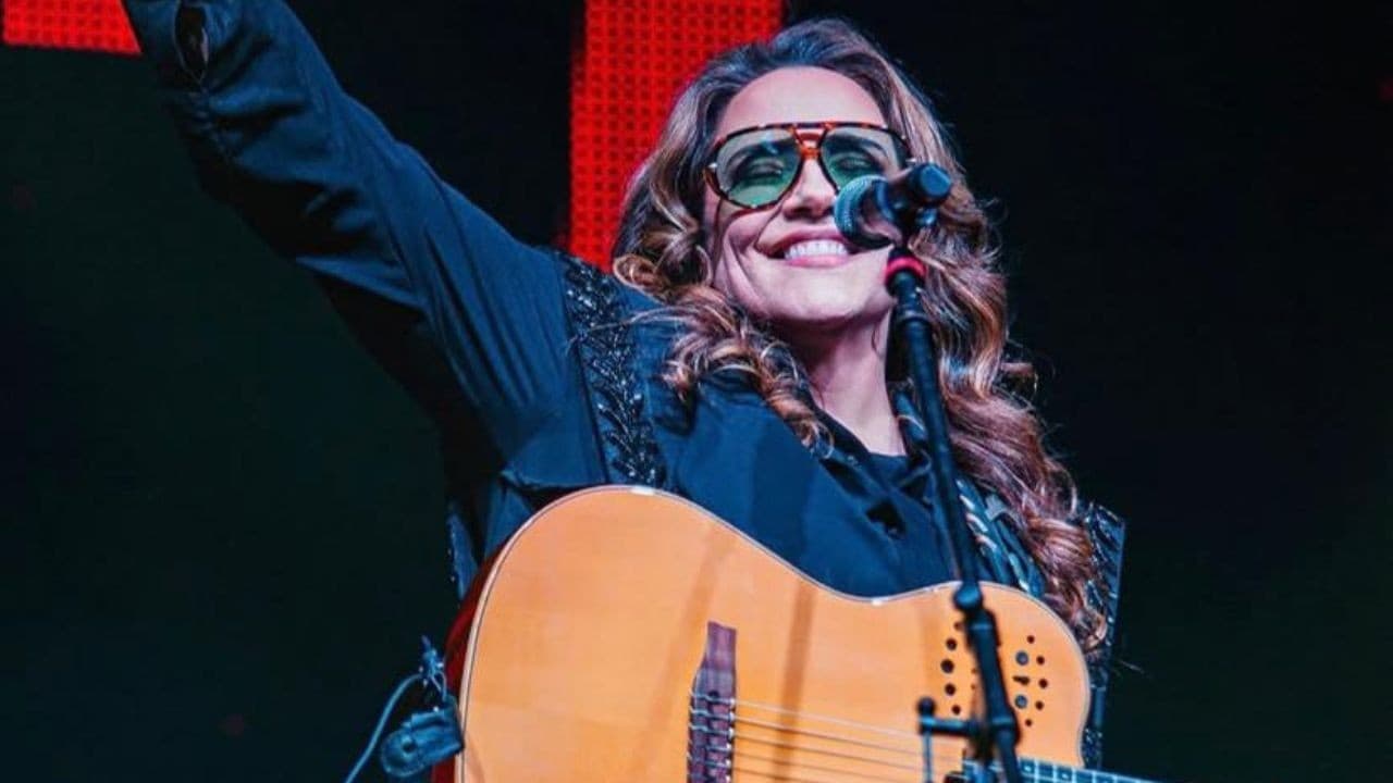 Cantora Ana Carolina segura violão em palco iluminado durante show da turnê 25 Anas.