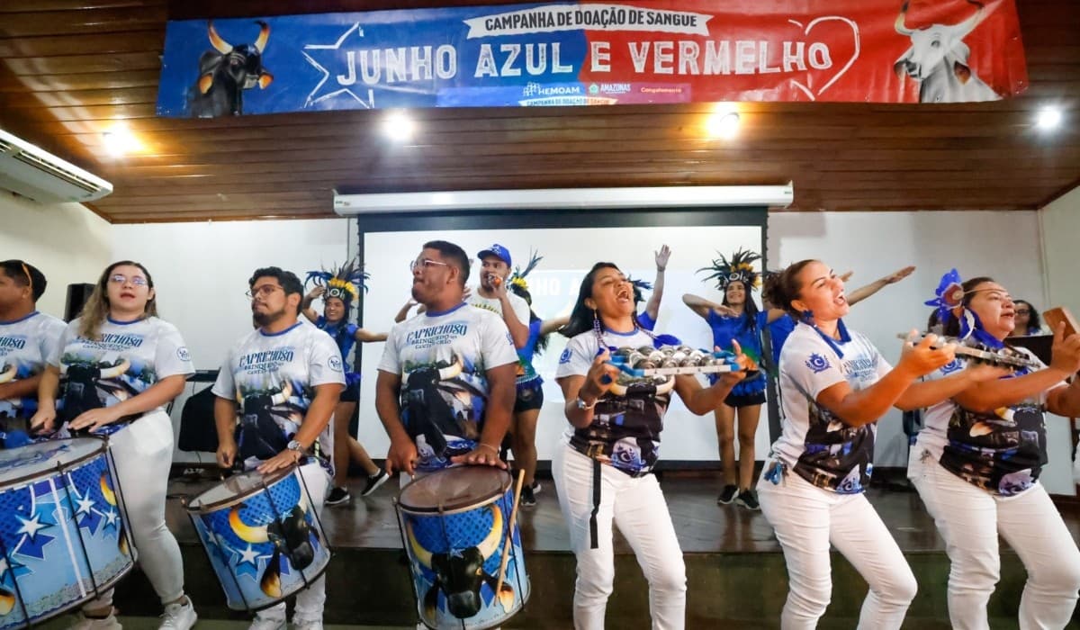 Pessoa segura material para coleta de sangue ao lado de banner do Hemoam com referência ao Festival de Parintins.