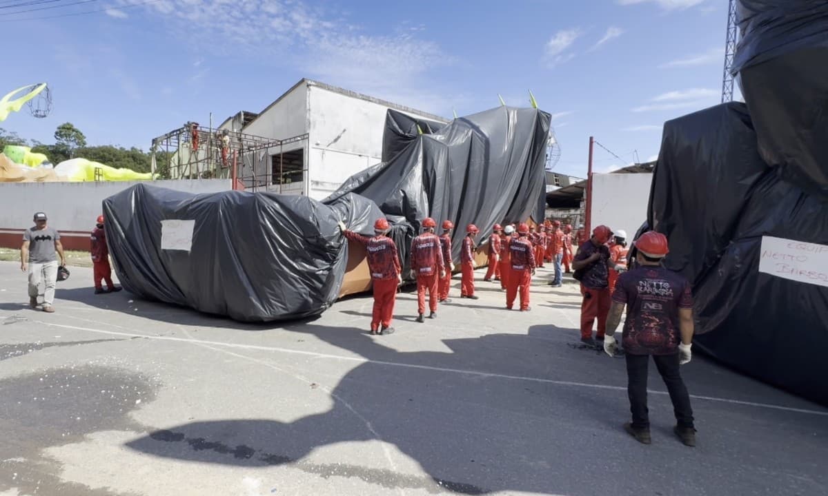 Caminhão transporta estrutura gigante de alegoria pelas ruas de Parintins sob sol da manhã.