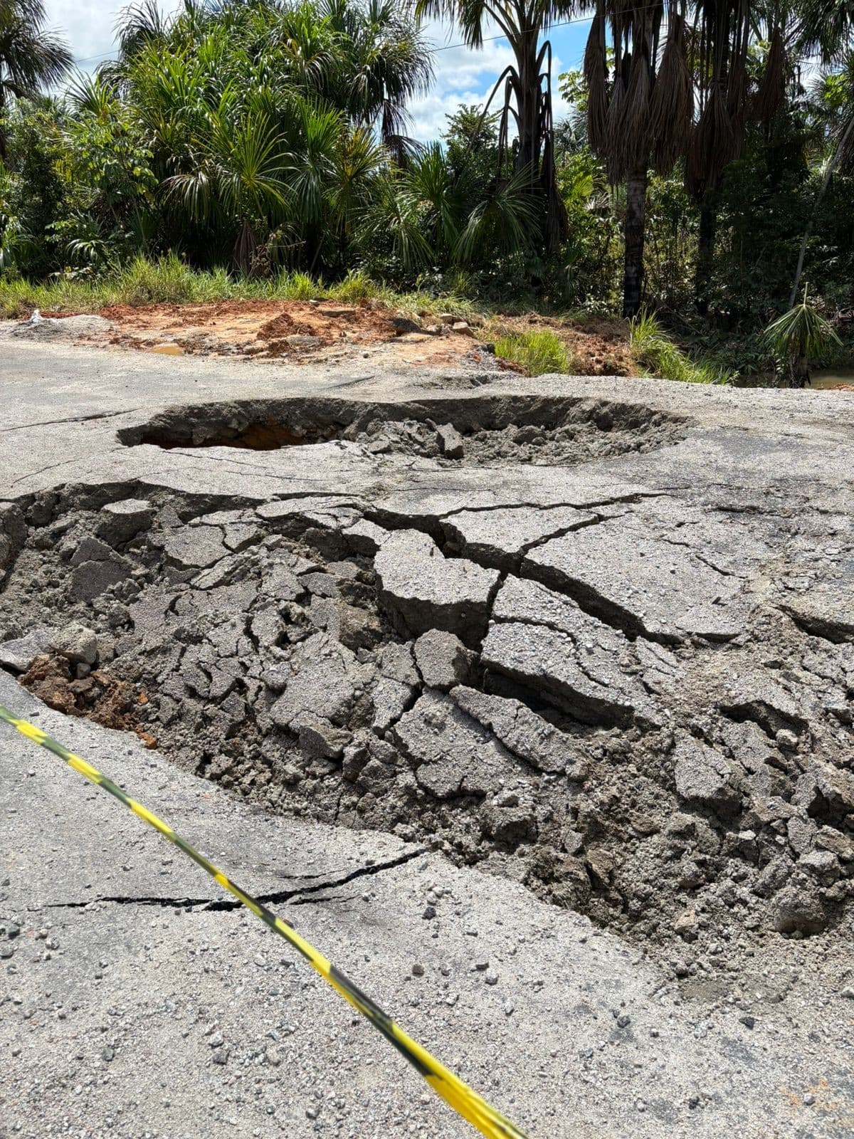 Trecho da rodovia BR-364 com asfalto deteriorado e placas de sinalização na margem da estrada no Acre.