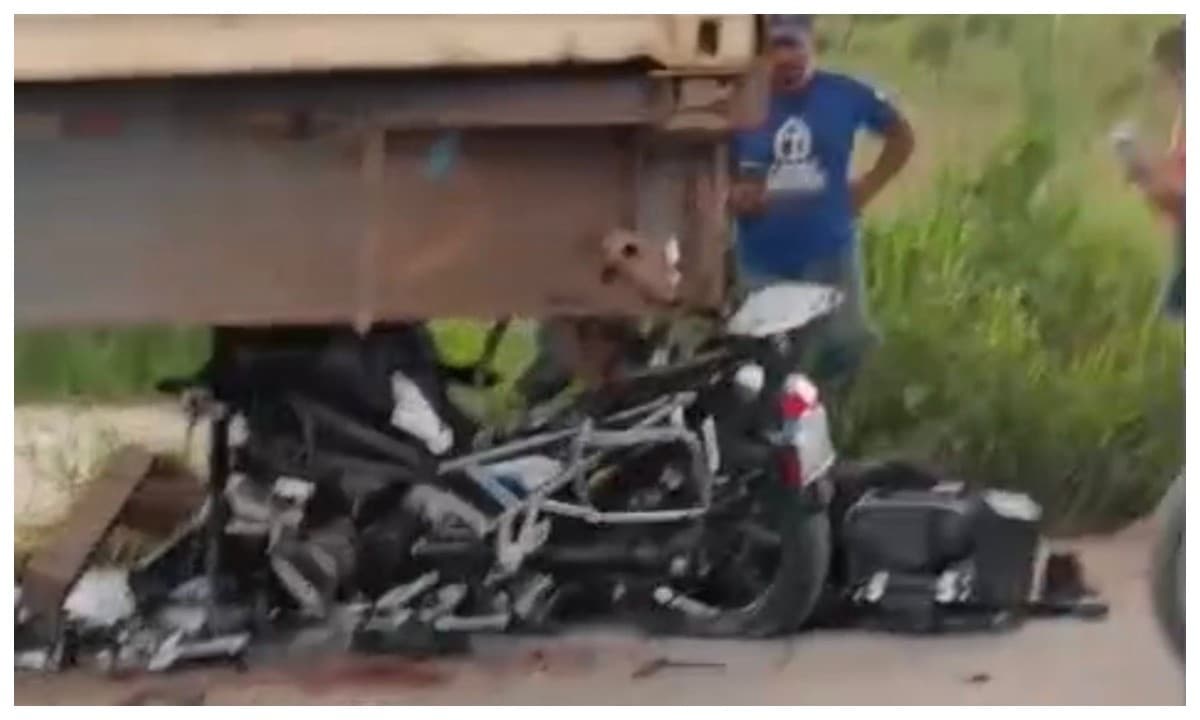 Restos de motocicleta destruída caídos no asfalto após colisão com caminhão.