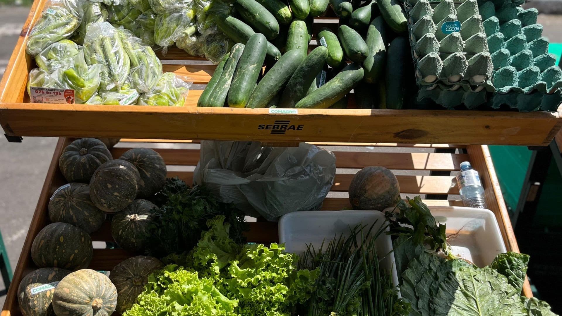 Banca de feirante com farinha de mandioca, frutas regionais e mel em potes expostos sobre mesa.