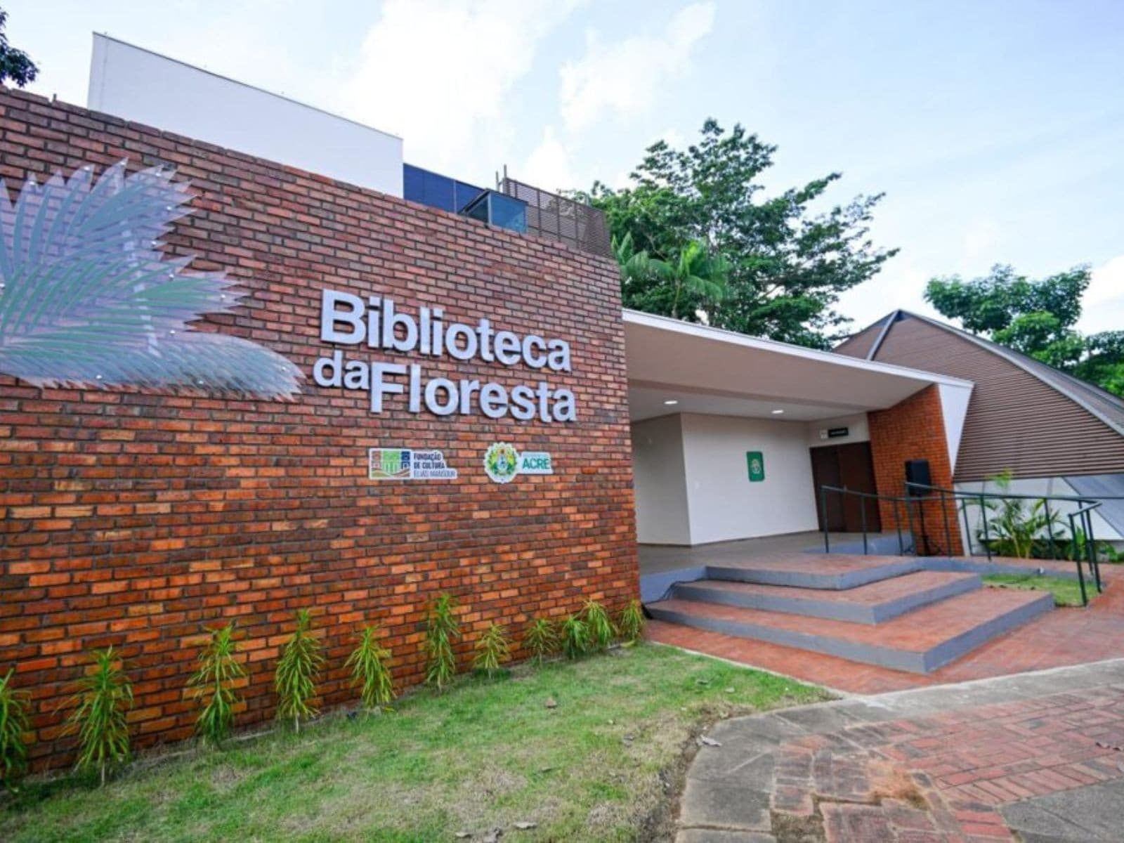 Pessoas circulam na área de leitura da Biblioteca da Floresta, em Rio Branco, com livros e mesas de estudo ao fundo.