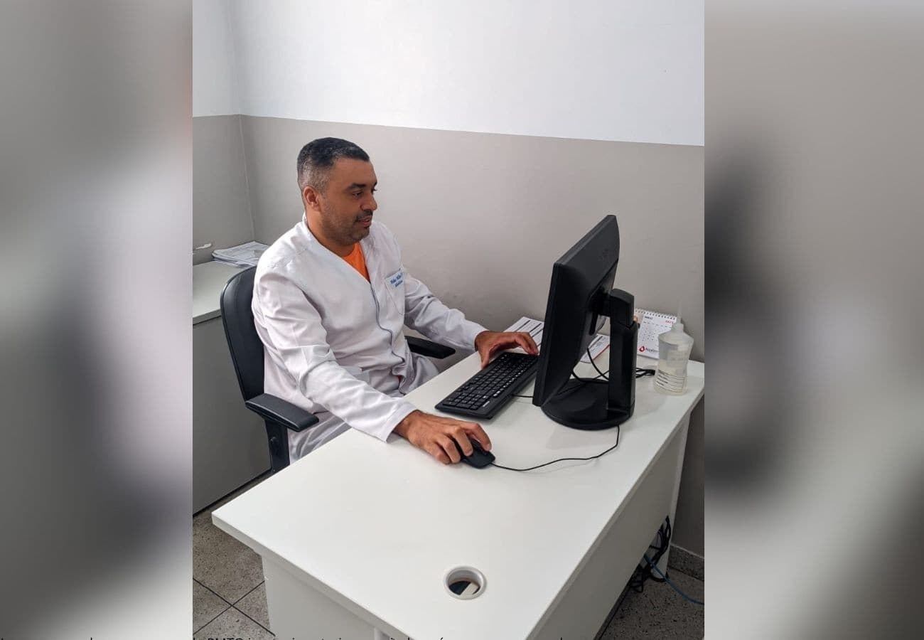 Estudante de medicina lê livro em mesa com cadernos e canetas espalhadas.