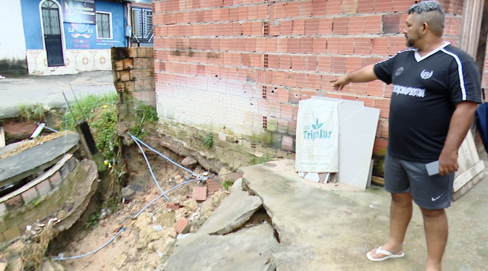 Rua com buraco e erosão ao lado de residência em Manaus.