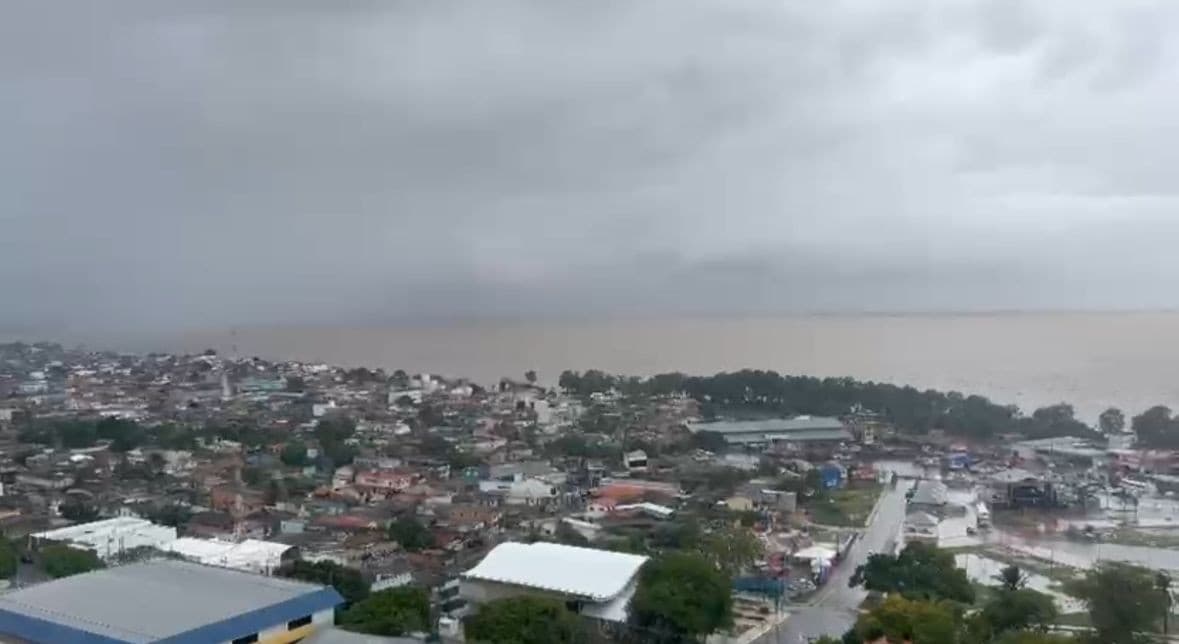 Rua de bairro em Macapá com asfalto molhado após chuva e nuvens cinzas no céu.