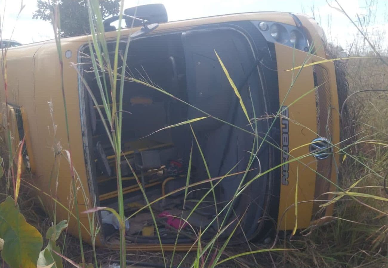 Ônibus escolar tombado na lateral da rodovia em região de campo.