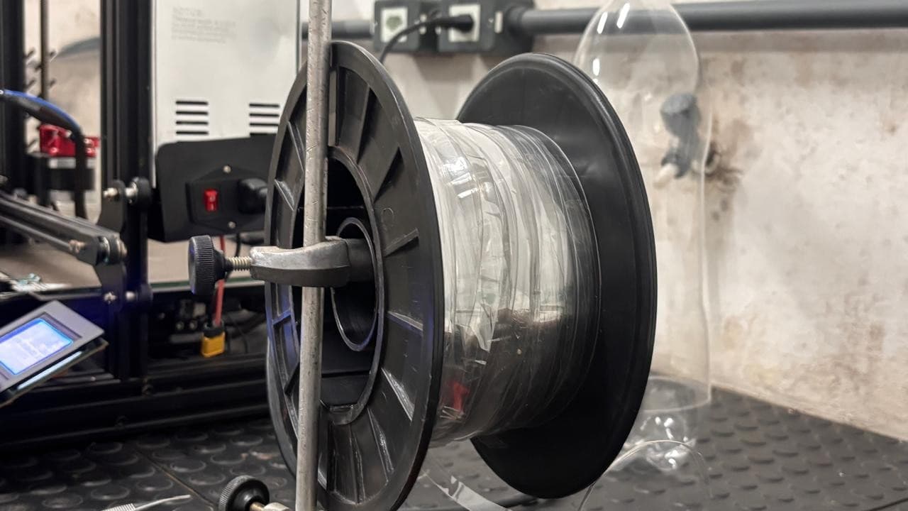 Estudantes observam impressora 3D funcionando com filamento de plástico reciclado em laboratório escolar.