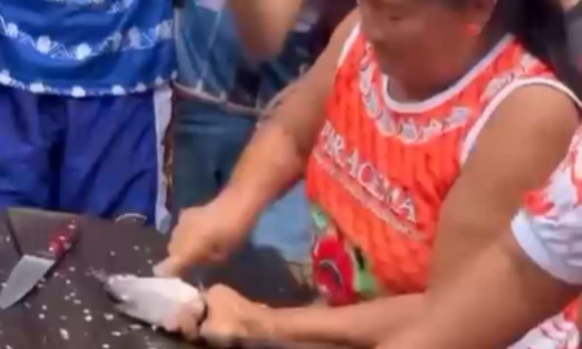 Mãos de ribeirinho limpam jaraqui em mesa de madeira durante competição no Amazonas.