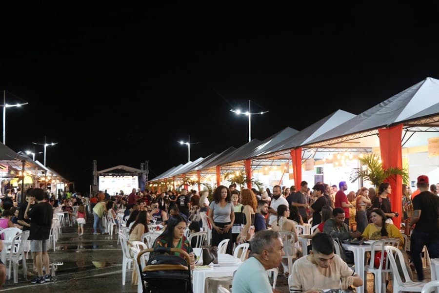 Prato colorido servido em tenda de festival ao ar livre com iluminação decorativa e bandeiras.