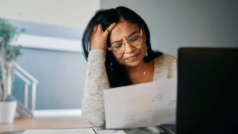 Pessoa segura cartões de crédito e calculadora em mesa de escritório.