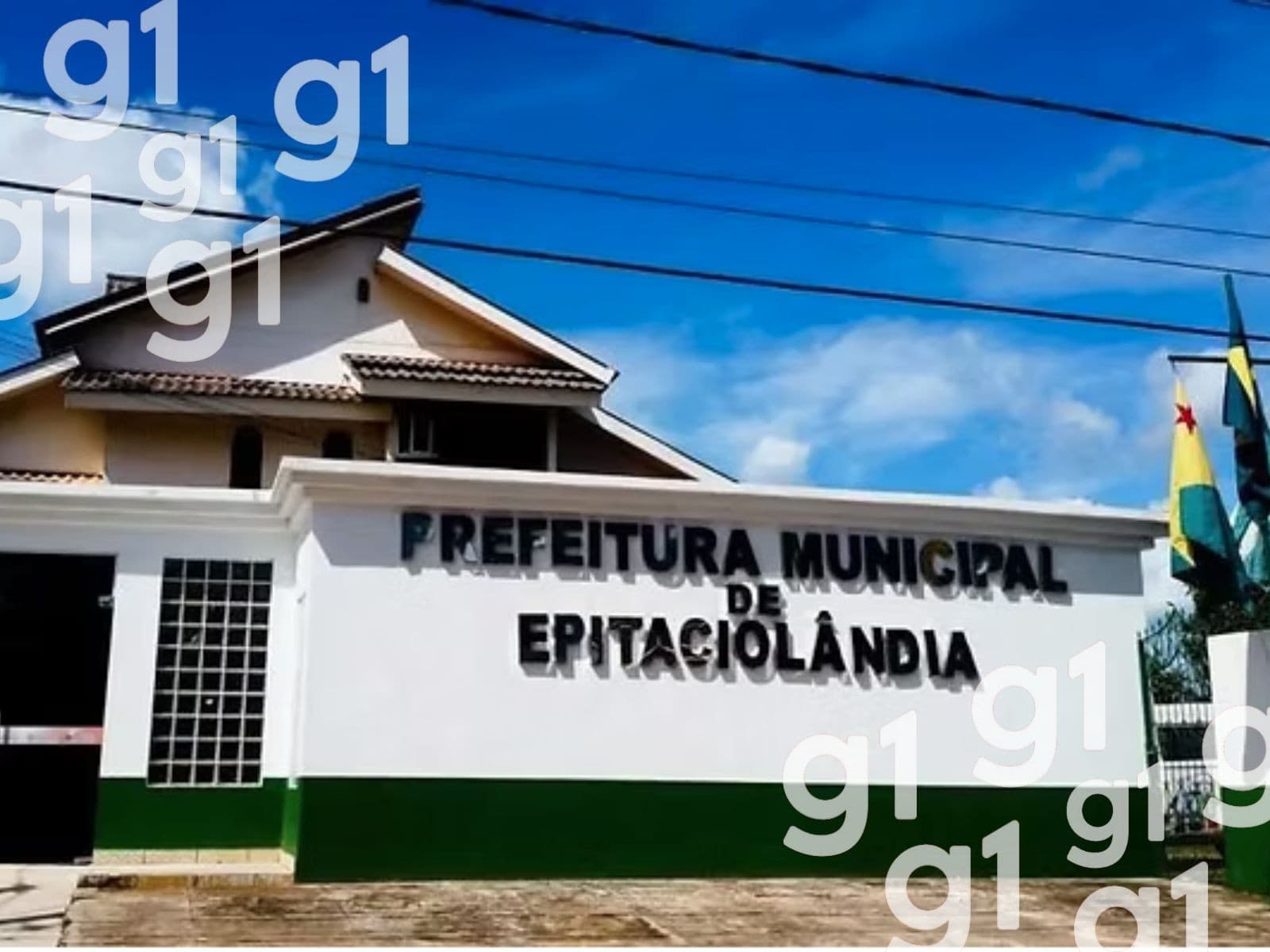 Prédio da Prefeitura de Epitaciolândia com bandeiras do Brasil e do Acre hasteadas em dia de sol.