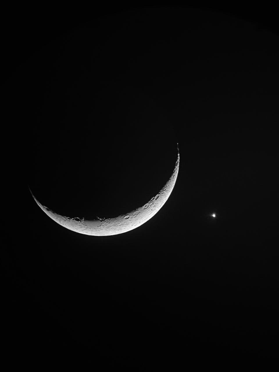 Lua crescente e ponto brilhante de Vênus visíveis no céu noturno escuro.