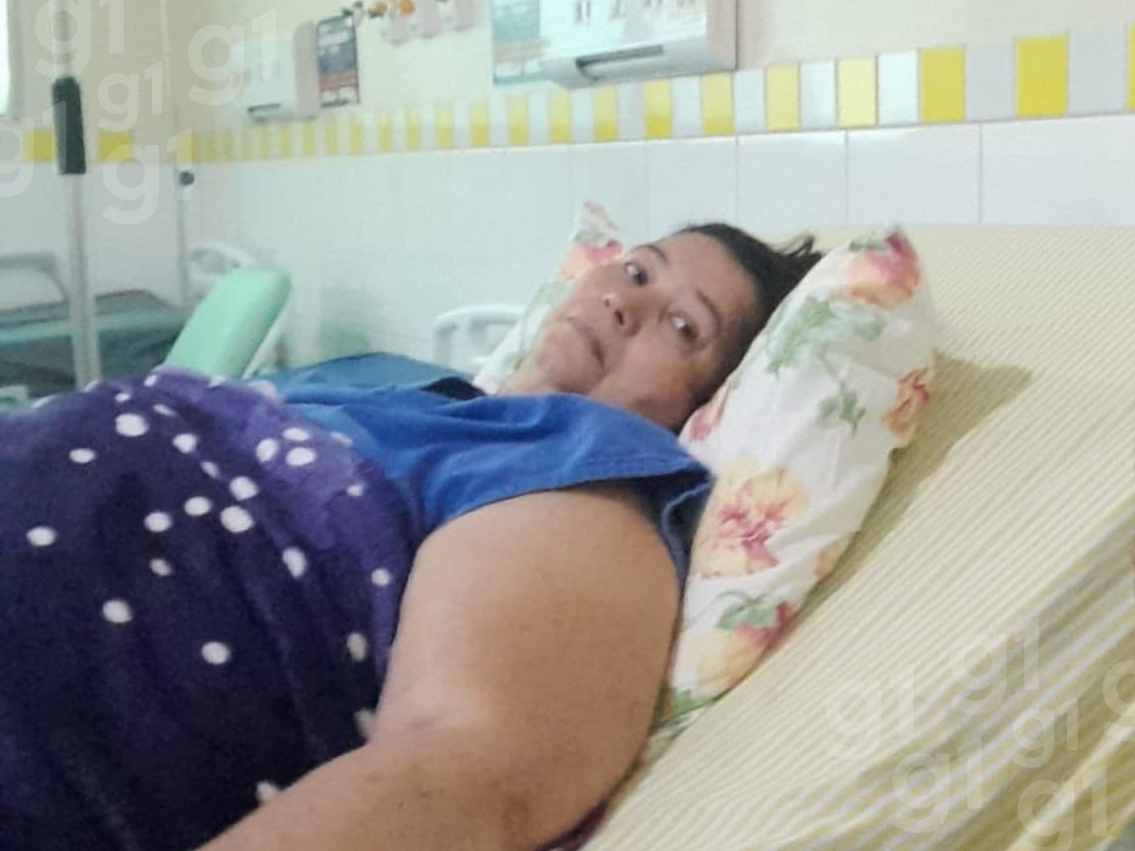 Mulher toca o pescoço delicadamente em frente à janela de uma casa simples.