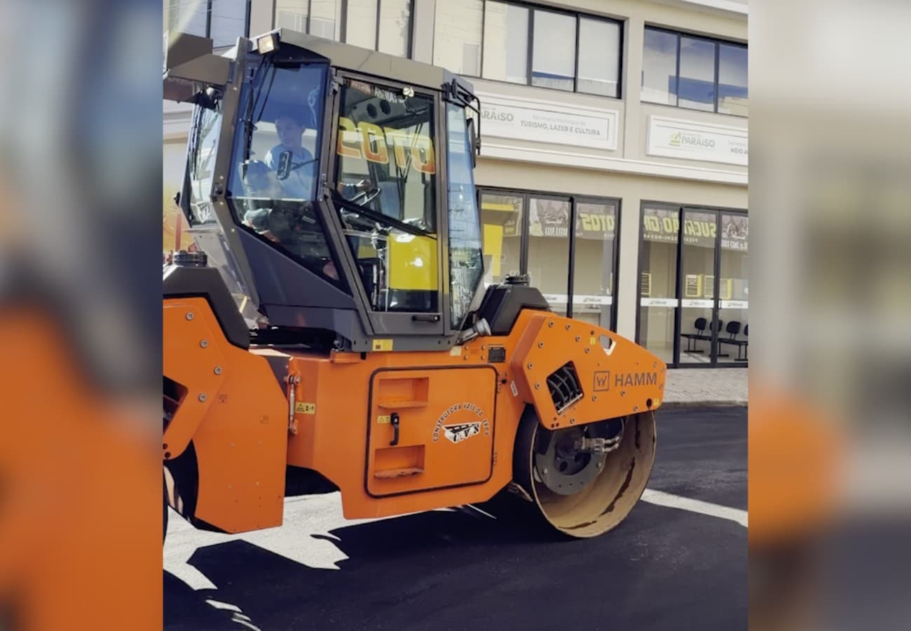 Mulher de bonet opera máquina amarela de construção civil sob sol forte em canteiro de obras.