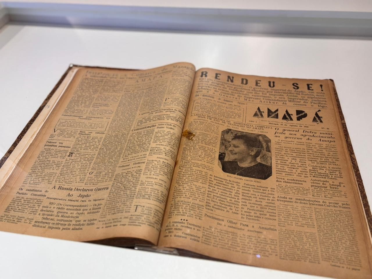 Máquina de impressão antiga exposta ao lado de terminal digital com jornais históricos.