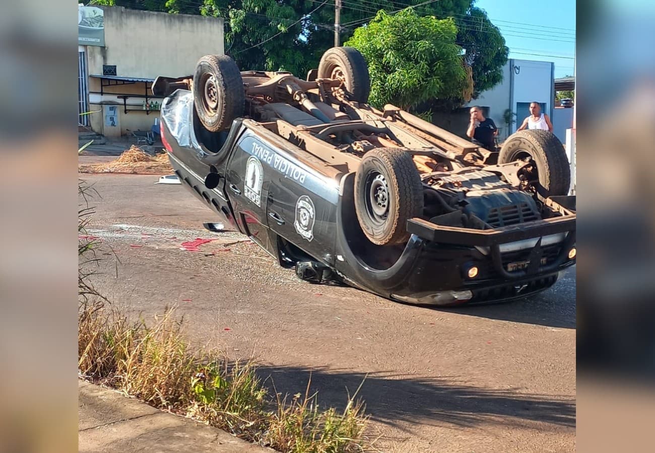 Viatura da Polícia Penal tombada com rodas para cima no asfalto do cruzamento.