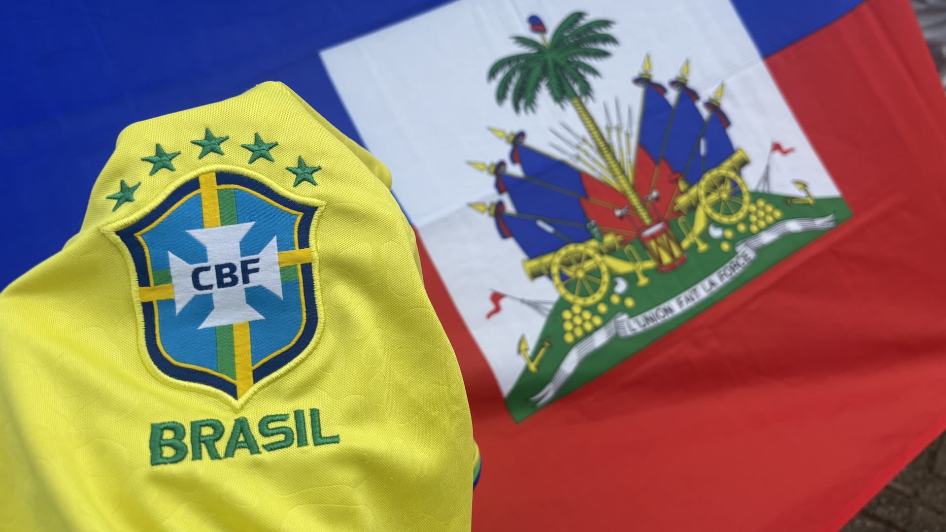 Bandeiras do Brasil e do Haiti lado a lado sobre mesa em sala de estar em Porto Velho.