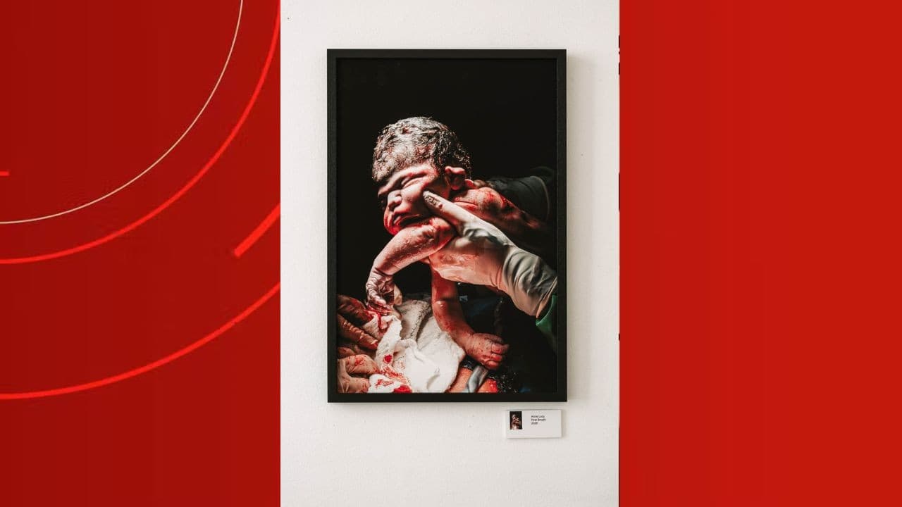 Fotografia artística em preto e branco captura o momento imediato após o nascimento, focando nas mãos da mãe e do bebê.