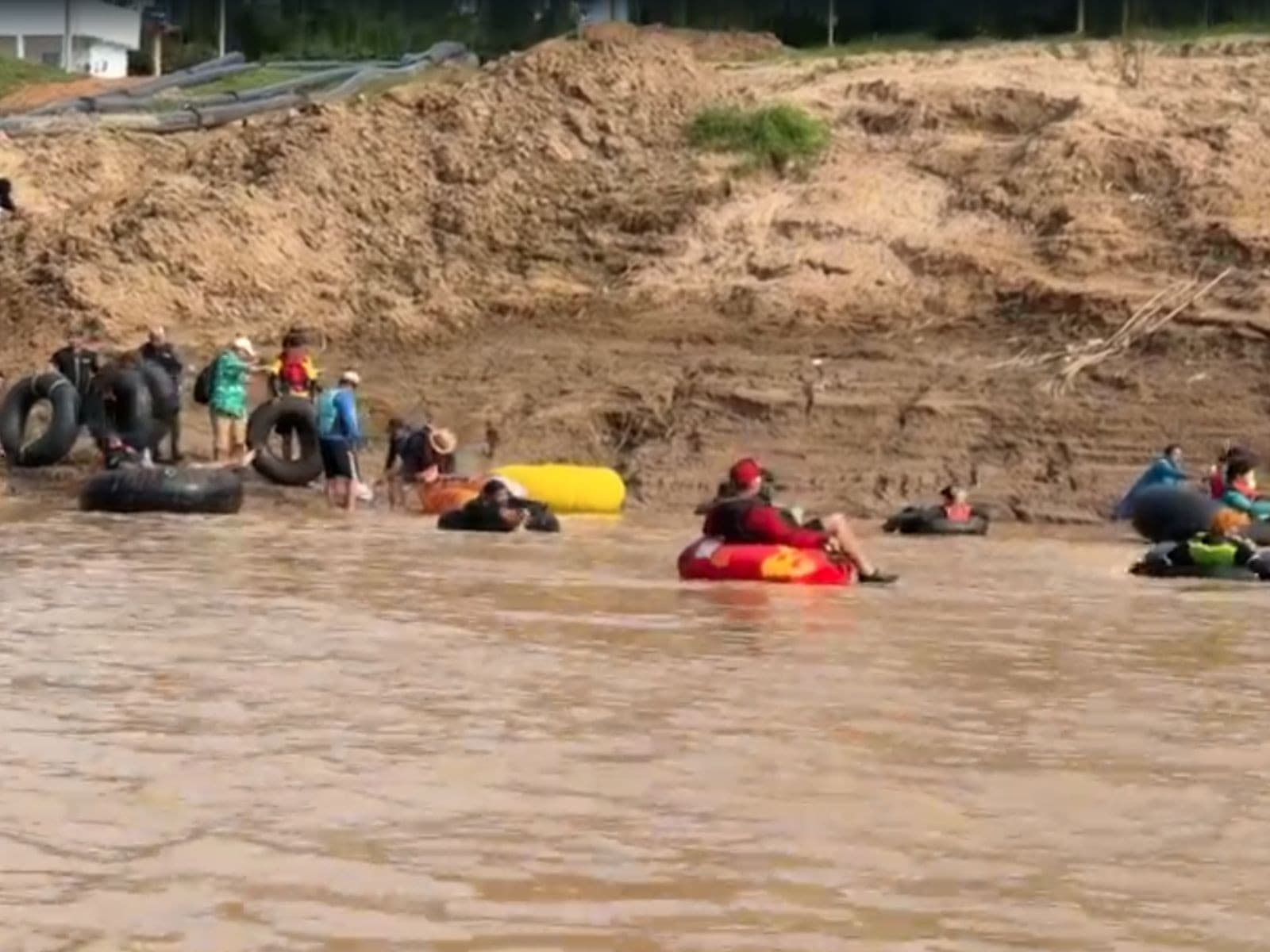 Grupo de pessoas em boias infladas flutuando no rio barrento cercado de vegetação ciliar em Rio Branco.