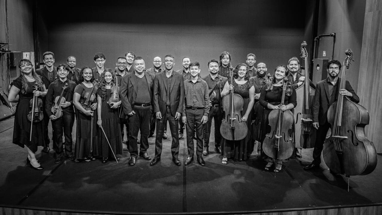 Maestro rege orquestra iluminada no palco do teatro ICBEU em Manaus.